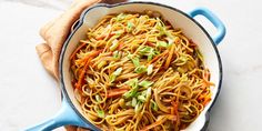 a pan filled with noodles and carrots on top of a white counter next to a wooden spoon