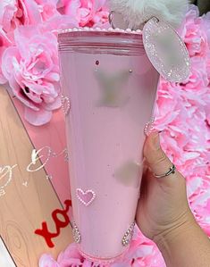 a person holding up a pink cup with hearts on it and flowers in the background