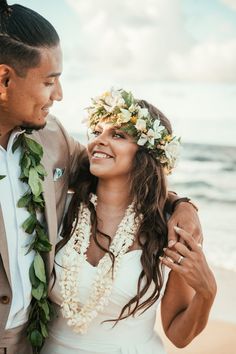 a man and woman standing next to each other on the beach with flowers in their hair