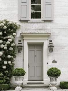 a white brick house with two large planters in front of the door and windows