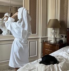 a person in a bathrobe standing on a bed looking at himself in the mirror