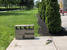 a cement box sitting on top of a sidewalk next to a green field and trees