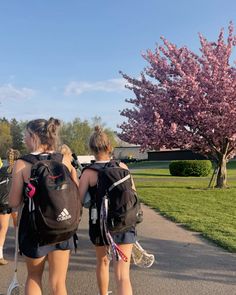 two girls are walking down the street with tennis rackets