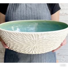 a person holding a bowl in their hands with white designs on the bottom and green inside