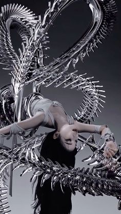 a woman is posing in front of a metal sculpture that looks like an alien creature