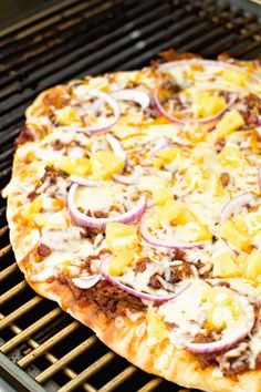 a pizza sitting on top of a grill covered in cheese and toppings with onions