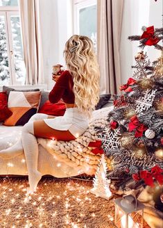 a woman sitting on top of a couch next to a christmas tree in front of a window