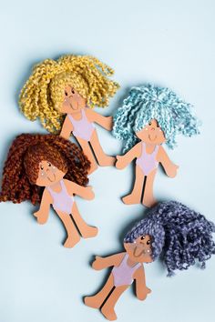 three wooden cutouts of people holding hands and wearing different colored wigs, on a blue background