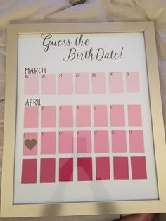 a person holding up a framed calendar with pink and red squares on it that says guess the birth date