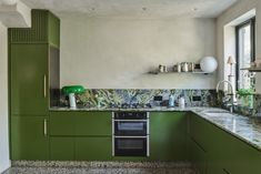 a kitchen with green cabinets and marble counter tops, along with a stove top oven