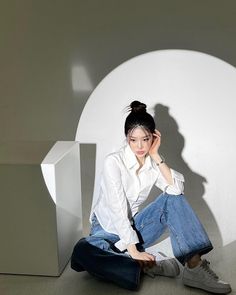 a woman sitting on the ground in front of a white wall with a shadow behind her