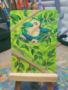 an easel with a painting of a bird sitting on a tree branch in front of paintbrushes