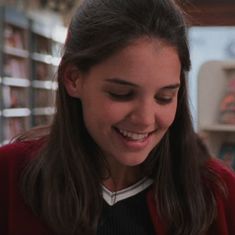 a girl smiles as she looks down at her cell phone in front of bookshelves