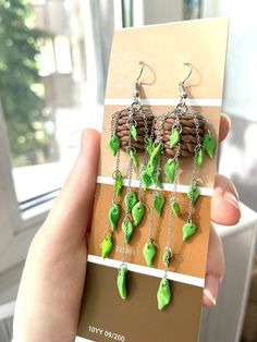 a person holding up a pair of earrings with green leaves hanging from it's hooks