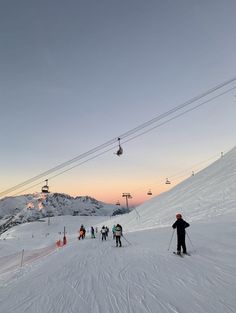 skiers and snowboarders at the bottom of a ski slope as the sun sets