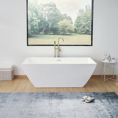 a large white bathtub sitting on top of a wooden floor next to a window