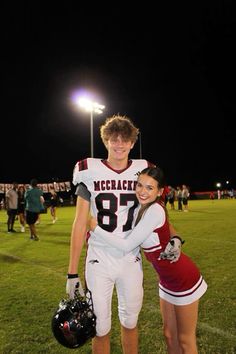 a man and woman in football uniforms posing for a photo on the field at night