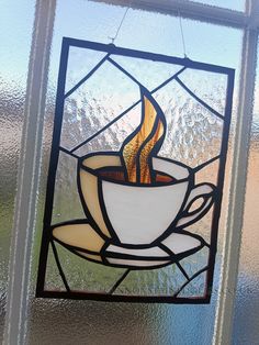 a stained glass window with a cup of coffee on it and the image of a flame coming out