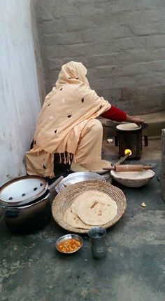 a woman sitting on the ground next to pots and pans with food in them