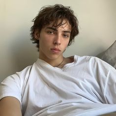 a young man sitting on top of a bed wearing a white shirt