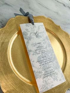 a gold plate with a white and gray menu card on it, sitting on a marble table