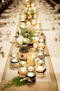 a long table with candles and vases on top of the tables is decorated with greenery