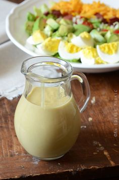 a glass pitcher filled with liquid next to a plate of salad on a wooden table