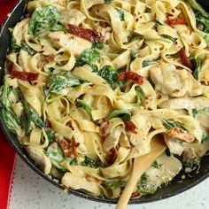 a skillet filled with pasta and spinach on top of a red table cloth