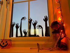 a window with halloween decorations on it and hands coming out from behind the windowsill