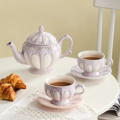 two cups of coffee and some croissants on a white table with lace doily