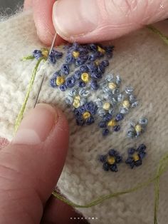 someone is stitching flowers on the side of a white knitted object with yellow and blue thread