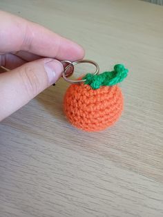 a hand holding a tiny crocheted keychain with a small orange on it