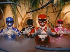 five power rangers sitting at a table with their hands in the air and one person standing behind them