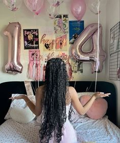 a woman with long hair sitting on a bed in front of balloons and letters hanging from the ceiling