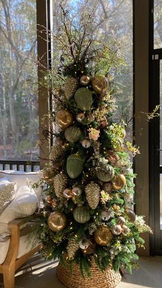 a christmas tree decorated with ornaments and greenery in front of a large glass window