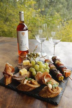 an assortment of appetizers and wine on a table with trees in the background