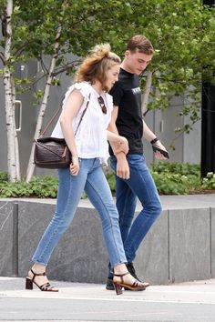 a man and woman walking down the street with one carrying a handbag in her other hand