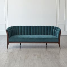 a green velvet couch sitting on top of a hard wood floor next to a white wall