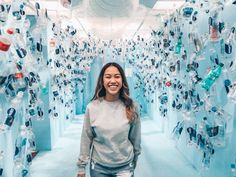 a woman standing in the middle of a room filled with water bottles and plastic cups