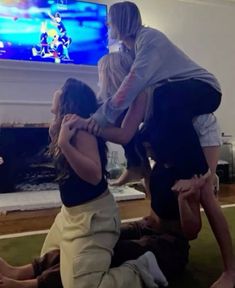 four people are sitting on the floor in front of a flat screen tv, and one person is holding onto another woman's leg