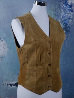 This vintage golden tan suede vest closes in the front with five buttons, and has two jetted pockets. The fully lined honey-colored pointed-front waistcoat features figure-enhancing contour lines on the front and a full leather back with a slip belt and a chevron slit on the center hemline. Brand label: Clic Point Size: Label: M, 6 US, 10 UK Material: Suede leather Condition: Excellent --- M E A S U R E M E N T S --- Bust = 34 inches (86.36cm) Vest Length Front = 23 inches (58.42cm) Vest Length Contour Lines, Leather Waistcoat, Label M, Suede Vest, Golden Tan, Brand Label, 1970s Fashion, 1960s Fashion, Plaid Blazer