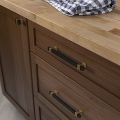 a wooden counter top with black handles and knobs next to a blue checkered dish towel