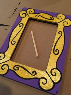 a purple and yellow frame with a pencil in the middle, on top of a cardboard box