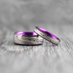 two wedding bands with purple inlays are sitting on top of a wooden table