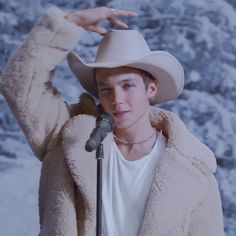 a man wearing a cowboy hat while standing in front of a snow covered mountain with a microphone