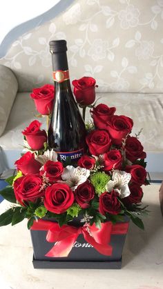 a bottle of wine sitting on top of a table next to red roses and greenery