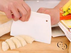 a person cutting up food on top of a wooden table next to books and bananas