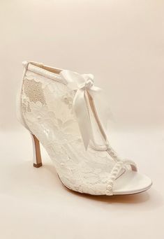 a pair of white high heeled shoes with lace on the side and bow at the ankle