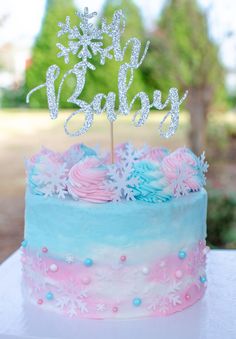 a blue and pink cake with frosting on top sitting on a table in front of trees