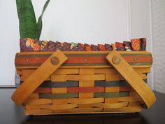 a wooden basket with two handles on top of a table next to a potted plant